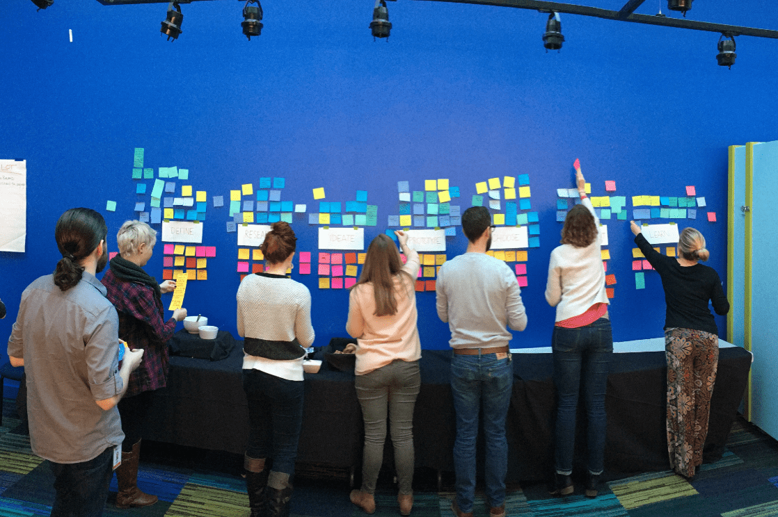 People putting multi-colored sticky notes on a blue wall.